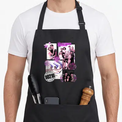 Tablier de cuisine noir avec un collage rose et violet de personnages et le logo 90210 en bas à gauche.