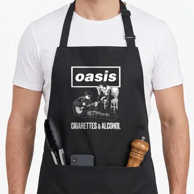 Tablier de cuisine noir avec logo Oasis et deux hommes illustrés en blanc, l'un jouant de la guitare, l'autre assis sur une chaise.