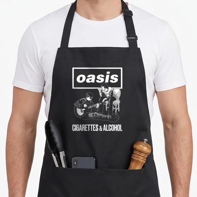 Tablier de cuisine noir avec logo Oasis et deux hommes illustrés en blanc, l'un jouant de la guitare, l'autre assis sur une chaise.