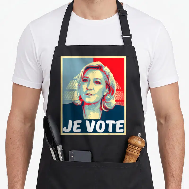 Tablier de cuisine noir avec portrait stylisé et texte Je Vote en grandes lettres blanches sur fond rouge et bleu.