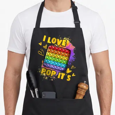 Tablier de cuisine noir avec un jouet pop it multicolore et le texte I love pop its en jaune.