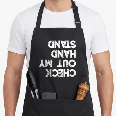 Tablier de cuisine noir avec inscription blanche inversée Check Out My Handstand Calisthenics en typographie usée.