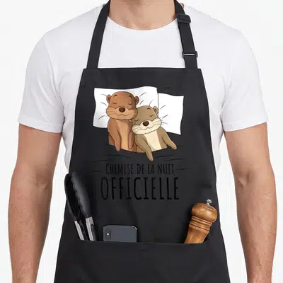 Tablier de cuisine noir avec deux loutres au lit et le texte « chemise de la nuit » imprimé en noir.
