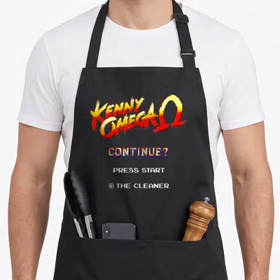 Tablier de cuisine noir avec logo Kenny Omega pixelisé rouge et jaune et texte continue press start en bas.
