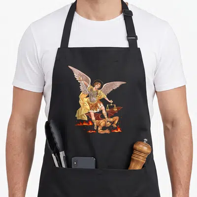 Tablier de cuisine noir avec illustration colorée de l'Archange Saint Michel vainquant un démon sur des flammes tout en tenant une balance dorée.