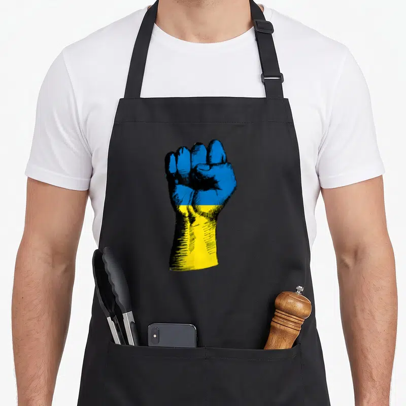 Tablier de cuisine noir avec un poing levé aux couleurs du drapeau ukrainien en style gravure.
