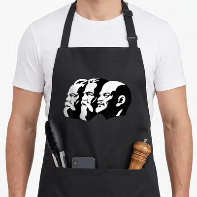 Tablier de cuisine noir avec trois visages masculins de profil imprimés en blanc, style graphique simplifié.