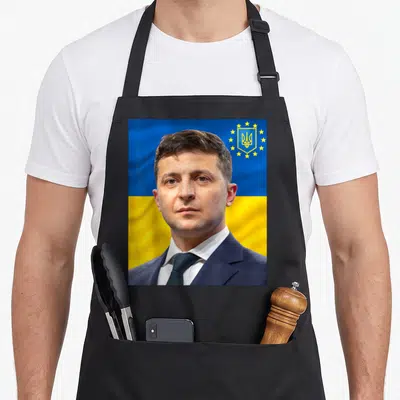 Tablier de cuisine noir avec portrait de Volodymyr Zelensky sur fond de drapeau ukrainien bleu et jaune.