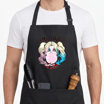 Tablier de cuisine noir avec Harley Quinn aux cheveux bicolores crachant une bulle rose sous l'inscription Mad Love.
