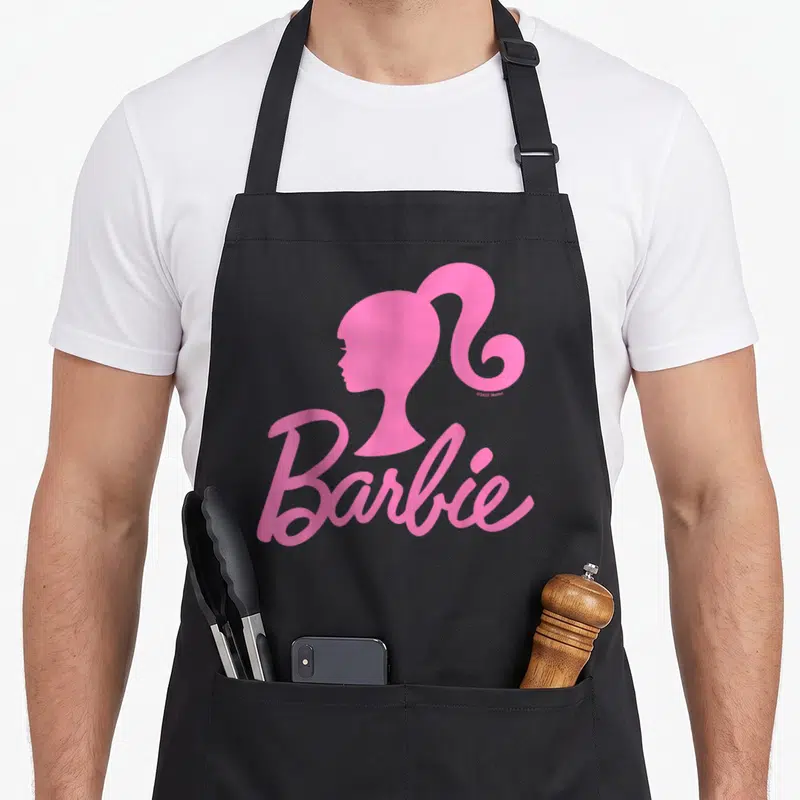 Tablier de cuisine noir avec le logo Barbie rose et le profil stylisé de la poupée en haut à droite.