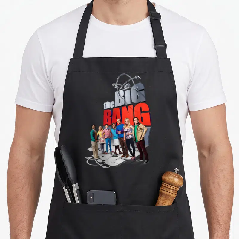 Tablier de cuisine noir avec le logo The Big Bang Theory et l'affiche des personnages principaux alignés.