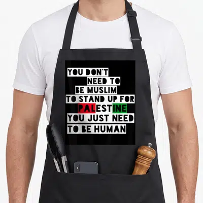 Tablier de cuisine noir avec inscription blanche et mots Palestine en rouge et vert sur fond noir uni.