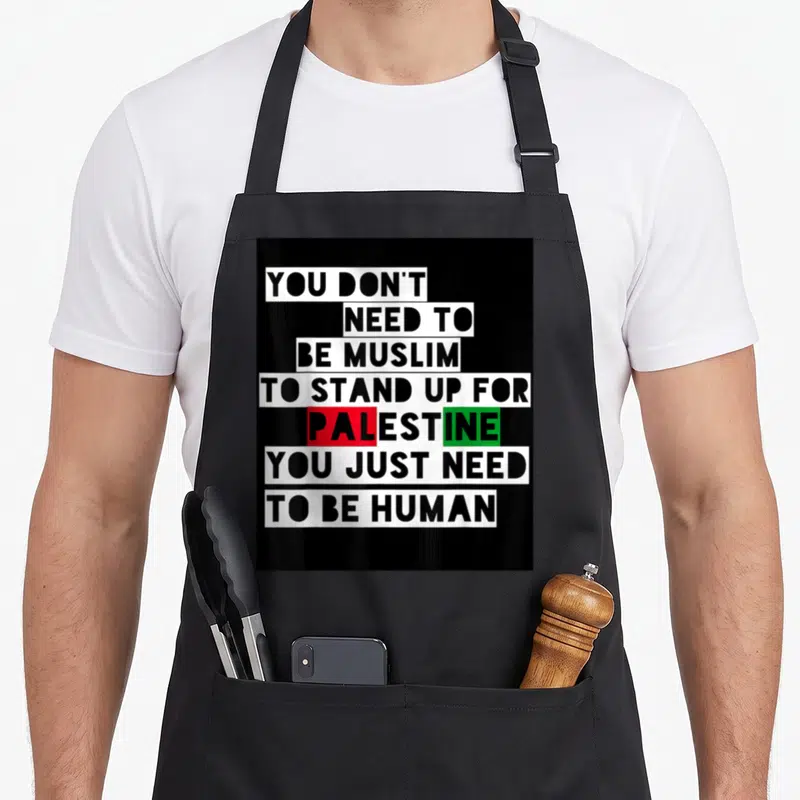 Tablier de cuisine noir avec inscription blanche et mots Palestine en rouge et vert sur fond noir uni.