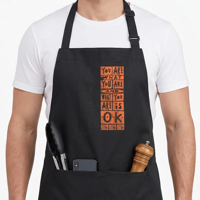 Tablier de cuisine noir avec personnage Fido Dido et texte orange You Are What You Are Is Ok.