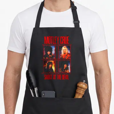 Tablier de cuisine noir avec le logo Mötley Crüe et quatre portraits encadrés de barbelés rouges sur fond gris.