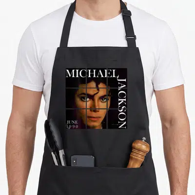 Tablier de cuisine noir avec portrait en grille de Michael Jackson et texte blanc June 1990 sur le devant.