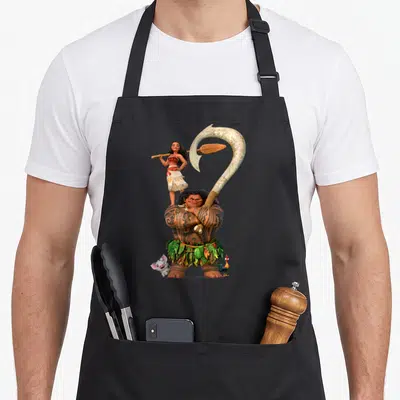 Tablier de cuisine noir avec Vaiana sur les épaules de Maui tenant un crochet géant et ses animaux.