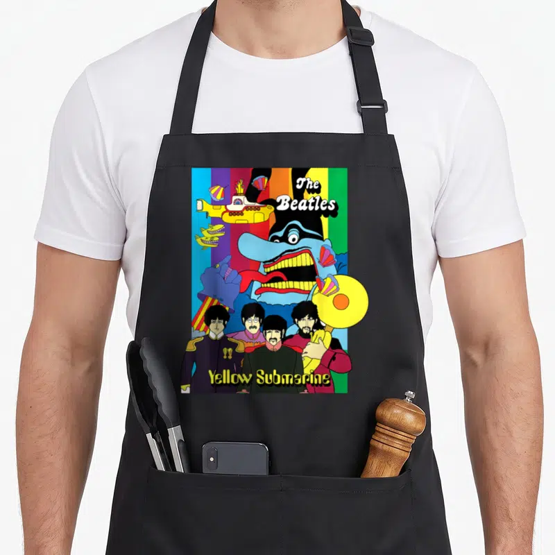 Tablier de cuisine noir avec illustration colorée des Beatles et du sous-marin jaune sur fond arc-en-ciel.