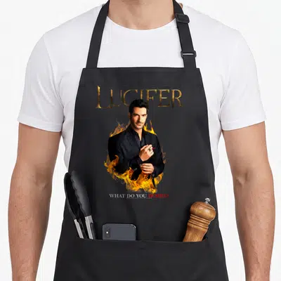 Tablier de cuisine noir avec une illustration de Lucifer en costume entouré de feu et du texte What Do You Desire.