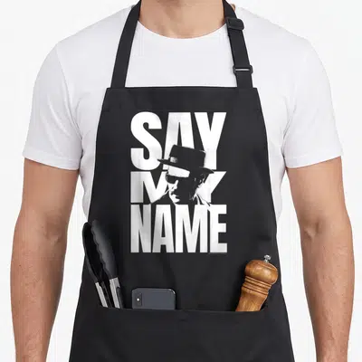 Tablier de cuisine noir avec illustration blanche de Walter White et le texte Say My Name en grosses lettres capitales.