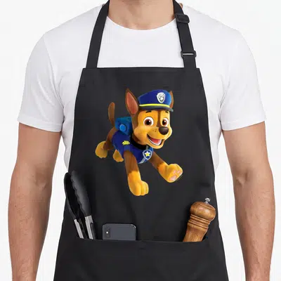 Tablier de cuisine noir avec Chase de la Patrouille des chiots en train de sauter en uniforme bleu et casquette de police.