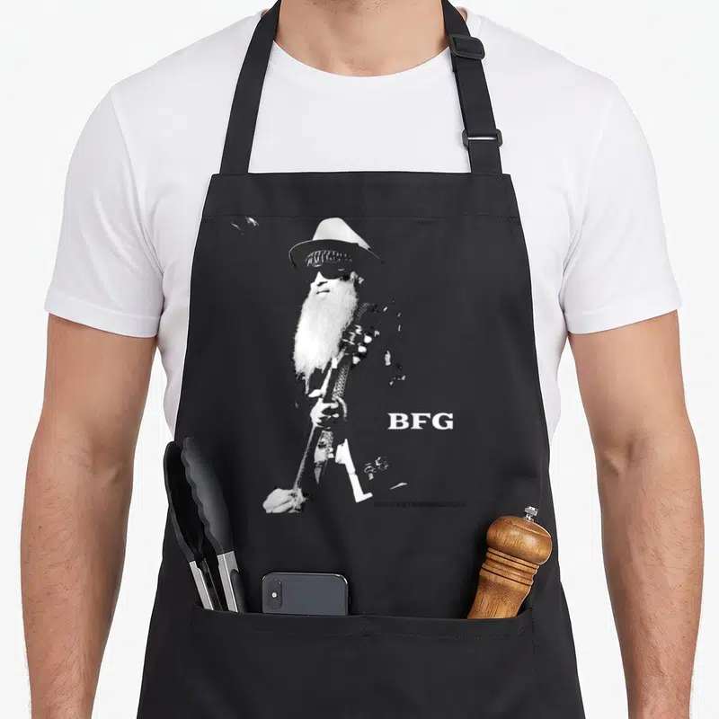 Tablier de cuisine noir avec illustration monochrome de Billy F Gibbons BFG tenant une guitare et portant un chapeau.