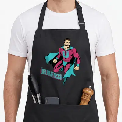 Tablier de cuisine noir avec illustration d'un super-héros barbu portant un U sur le torse et le mot Übermensch en bas à gauche.