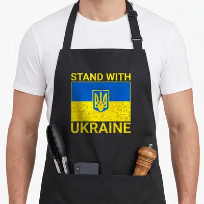 Tablier de cuisine noir avec drapeau Ukraine et texte Stand With Ukraine en jaune et bleu.