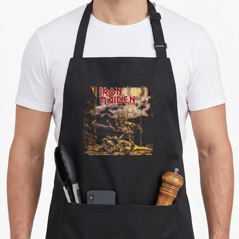 Tablier de cuisine noir avec illustration d'Eddie et le logo Iron Maiden sur fond urbain.