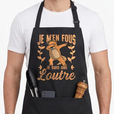 Tablier de cuisine noir avec une illustration orange d'une loutre effectuant un dab entourée de feuilles stylisées et du texte Je m'en fous je suis une loutre.