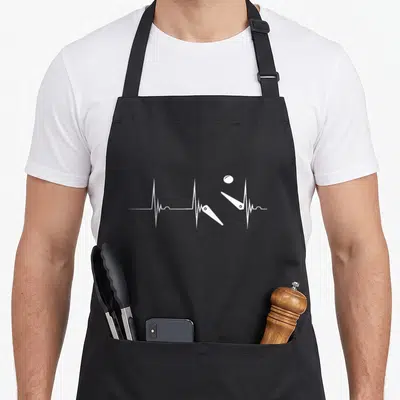 Tablier de cuisine noir avec un motif blanc représentant une ligne de battement de cœur transformée en flippers et boule de pinball.