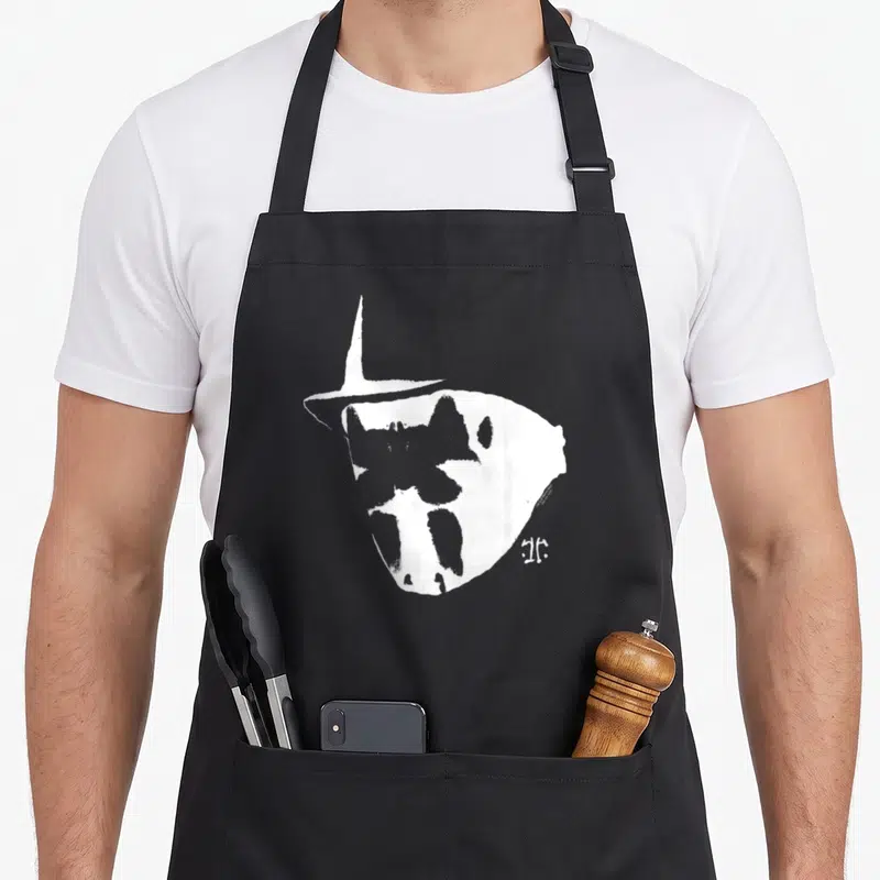 Tablier de cuisine noir avec illustration blanche du masque de Rorschach et signature artistique à côté.
