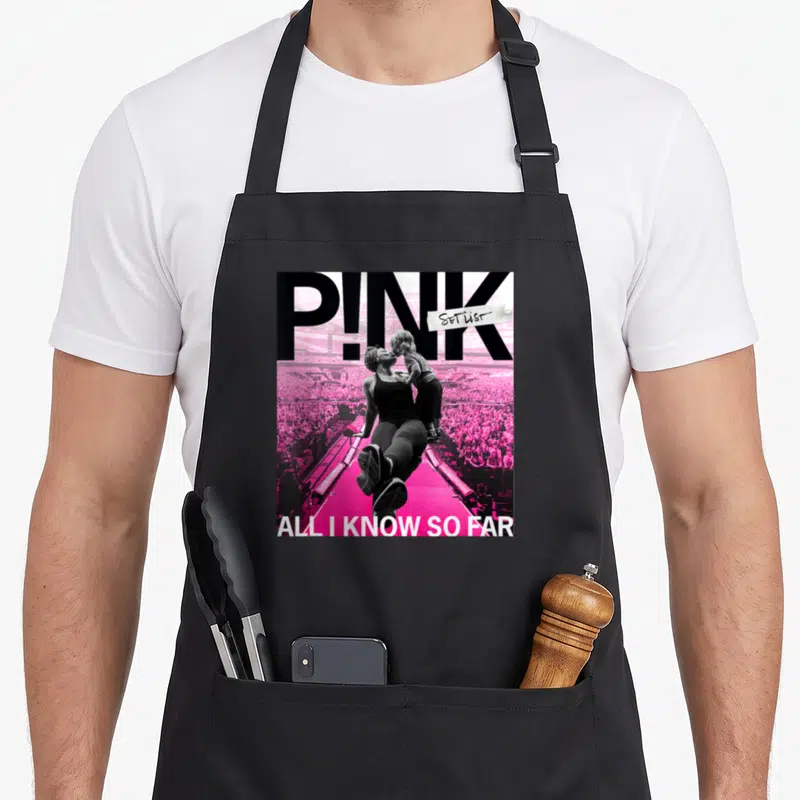 Tablier de cuisine noir avec illustration rose montrant P.NK tenant un enfant sur scène devant une foule.