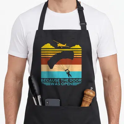 Tablier de cuisine noir avec illustration vintage d'un avion et d'un parachutiste sur fond de bandes colorées.