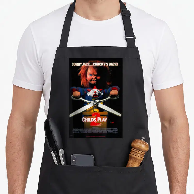 Tablier de cuisine noir avec l'image du poupée Chucky tenant des ciseaux sortant d'une boîte à musique.