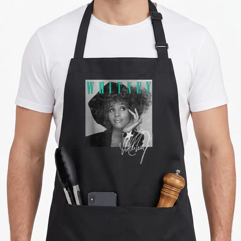 Tablier de cuisine noir avec portrait Whitney Houston, texte turquoise et signature blanche avec étoile.