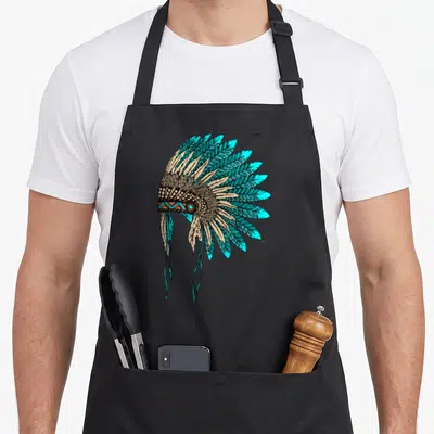 Tablier de cuisine noir avec une coiffe de plumes turquoise et des motifs tribaux colorés imprimée au centre.