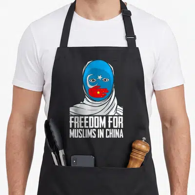 Tablier de cuisine noir avec illustration d'un visage masqué bleu et texte blanc sur fond uni.