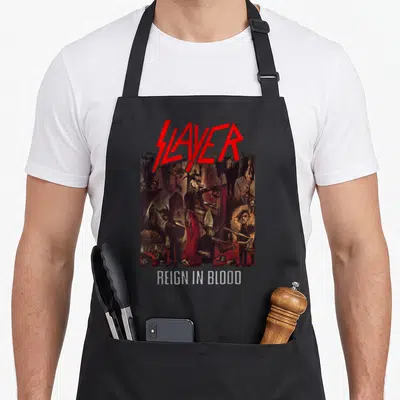 Tablier de cuisine noir avec logo Slayer rouge et illustration Reign in Blood sombre et macabre.
