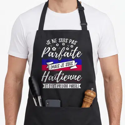 Tablier de cuisine noir avec l'inscription Je ne suis pas parfaite mais je suis Haïtienne sur fond de drapeau national.