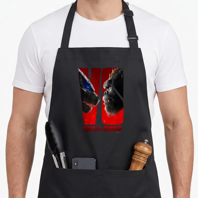 Tablier de cuisine noir avec une illustration rouge et noire représentant Godzilla face à Kong dans le mot VS.