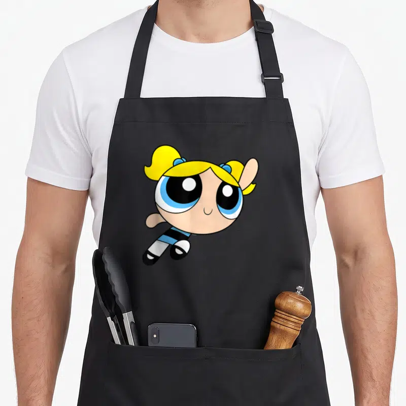 Tablier de cuisine noir avec illustration de Bubbles les Supéres aux cheveux blonds et yeux bleus en train de voler.