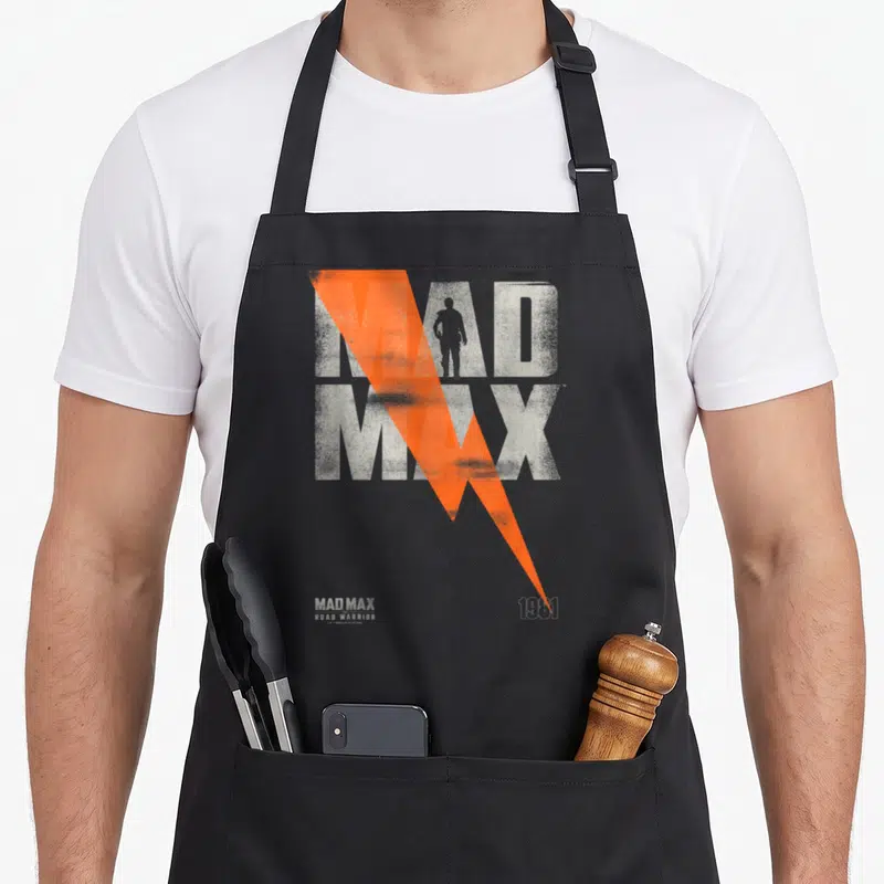 Tablier de cuisine noir avec l'affiche Mad Max Road Warrior 1981 et un éclair orange traversant le texte.