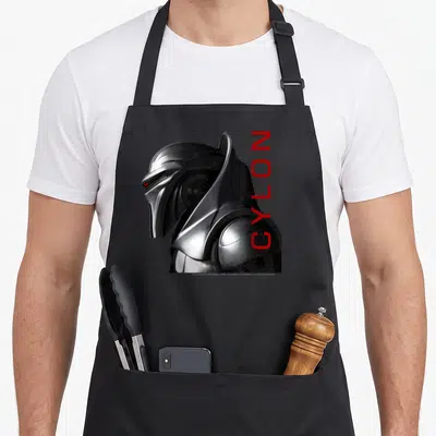 Tablier de cuisine noir avec le profil argenté d'un Cylon et le texte vertical rouge CYLON sur le côté droit.