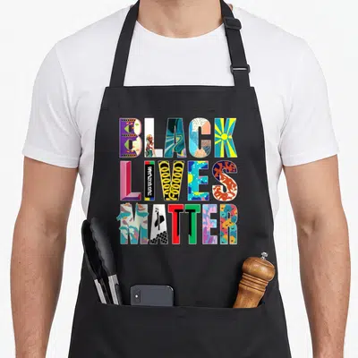 Tablier de cuisine noir avec le message Black Lives Matter composé de motifs artistiques multicolores et de symboles culturels distincts.