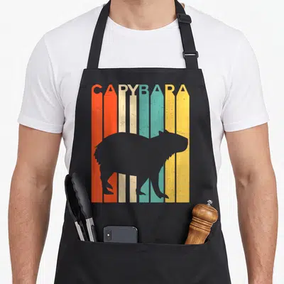 Tablier de cuisine noir avec silhouette de capybara sur bandes orange, crème et turquoise et le mot Capybara en haut.
