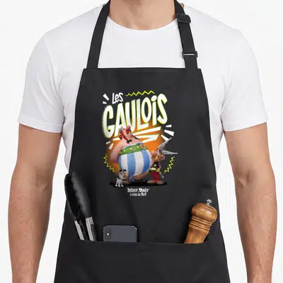 Tablier de cuisine noir avec Asterix Obelix et les mots Les Gaulois en typographie colorée 3D sur fond orange.