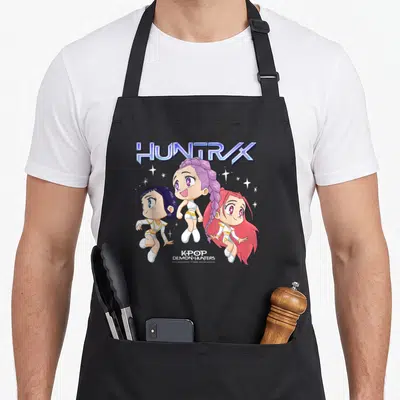 Tablier de cuisine noir avec les personnages Huntrix en style chibi et le titre Kpop Demon Hunters imprimé en bas.