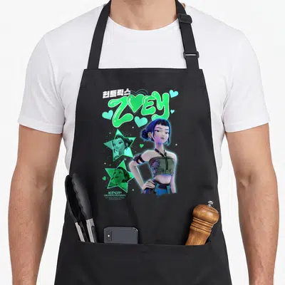 Tablier de cuisine noir avec l'illustration de Zoey Popstar, des étoiles vertes et le texte Huntrix Zoey en typographie stylisée.