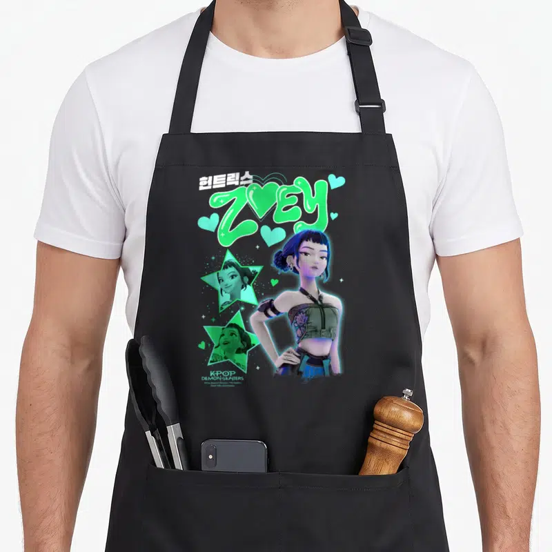 Tablier de cuisine noir avec l'illustration de Zoey Popstar, des étoiles vertes et le texte Huntrix Zoey en typographie stylisée.